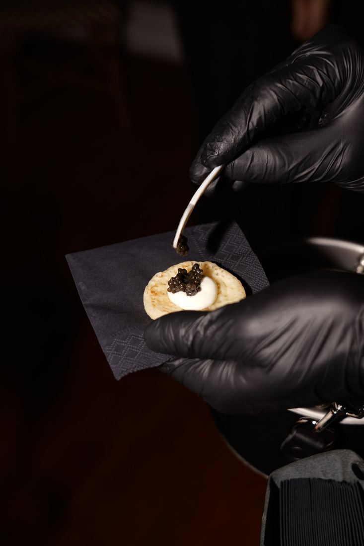 Mains gantées déposant le caviar sur un blini à la cuillère en nacre